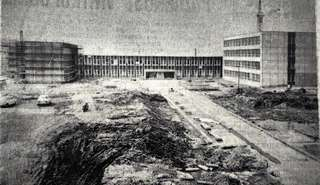 Černobílá fotografie zachycuje nedokončený areál ZŠ Milady Horákové, v popředí je vidět stavební materiál, hromady hlíny a částečně dokončené komunikace. V pozadí stojí dvě hlavní budovy.