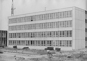 Černobílá fotografie čtyřpatrové obdélníkové budovy s mnoha okny, identifikovaná jako ZŠ Milady Horákové. V popředí je stavební materiál a zařízení, v pozadí je jeřáb této školy Hradec Králové.
